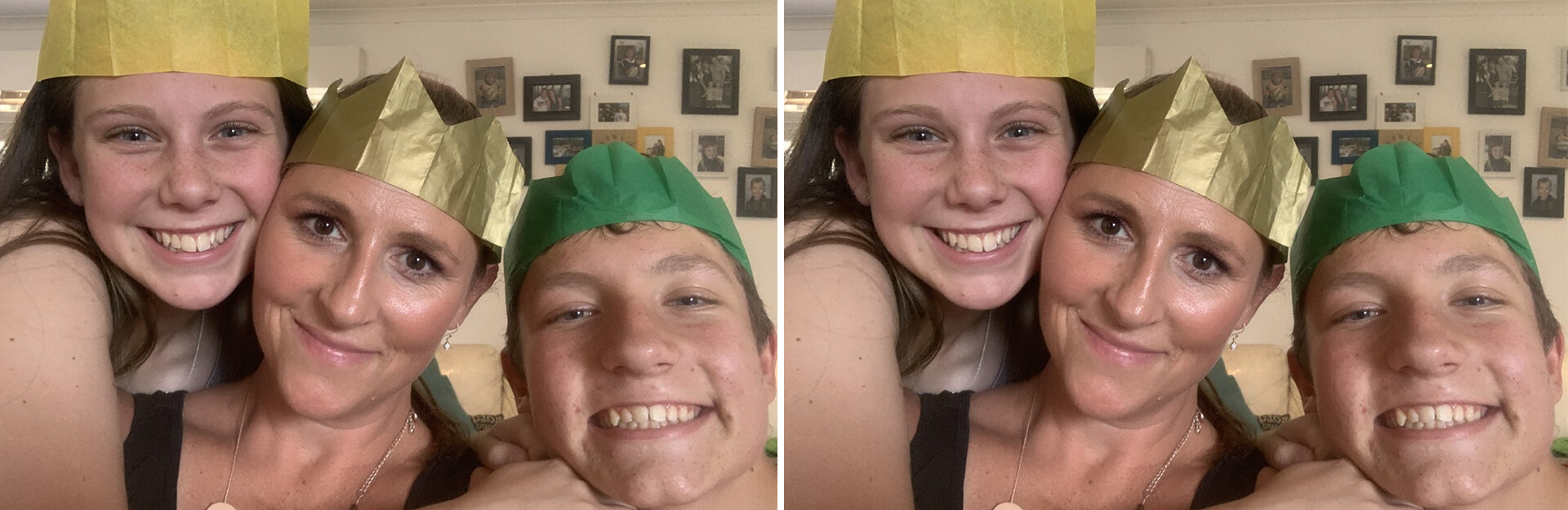 Three people smiling together, wearing colorful paper crowns, with a wall of framed photos in the background.
