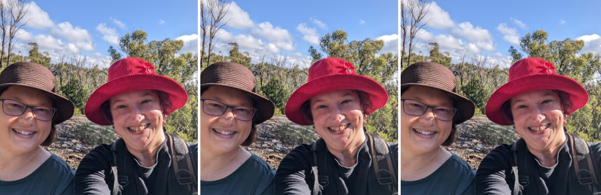 Two women smiling together outdoors, wearing hats, with greenery and a blue sky in the background.