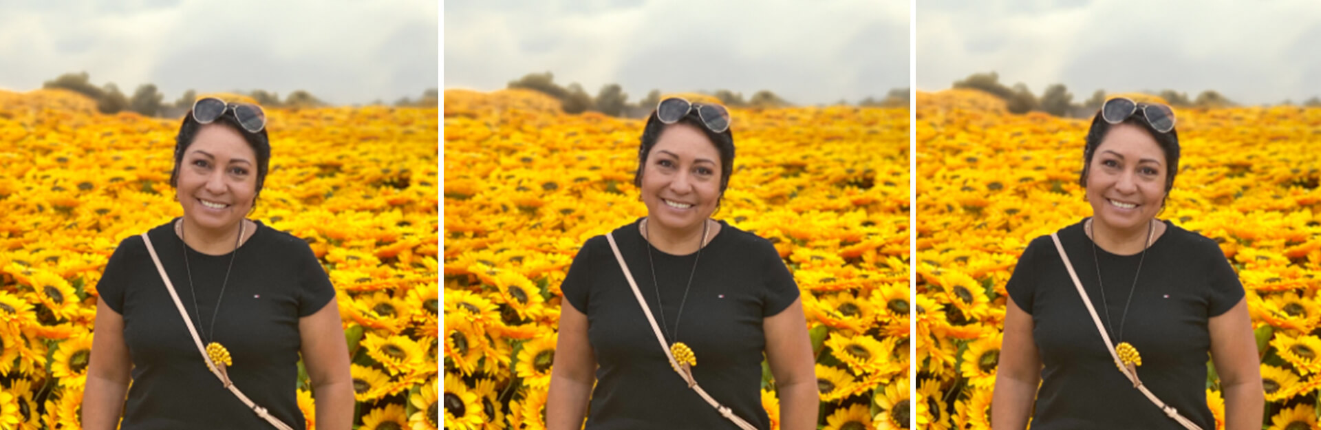 A woman smiles in front of a field of bright yellow sunflowers under a cloudy sky.
