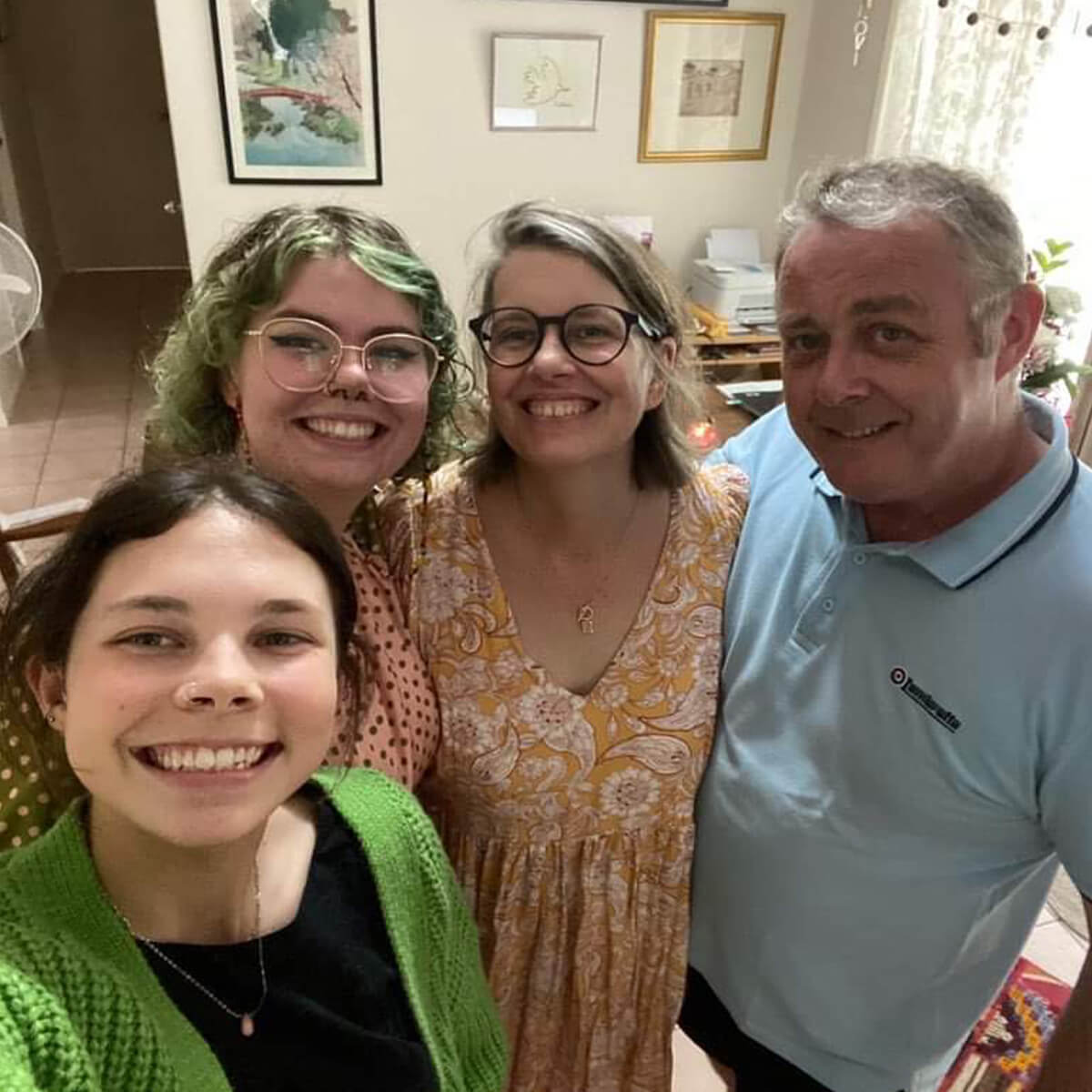 Four people smiling for a selfie in a cozy indoor setting with framed artwork in the background.