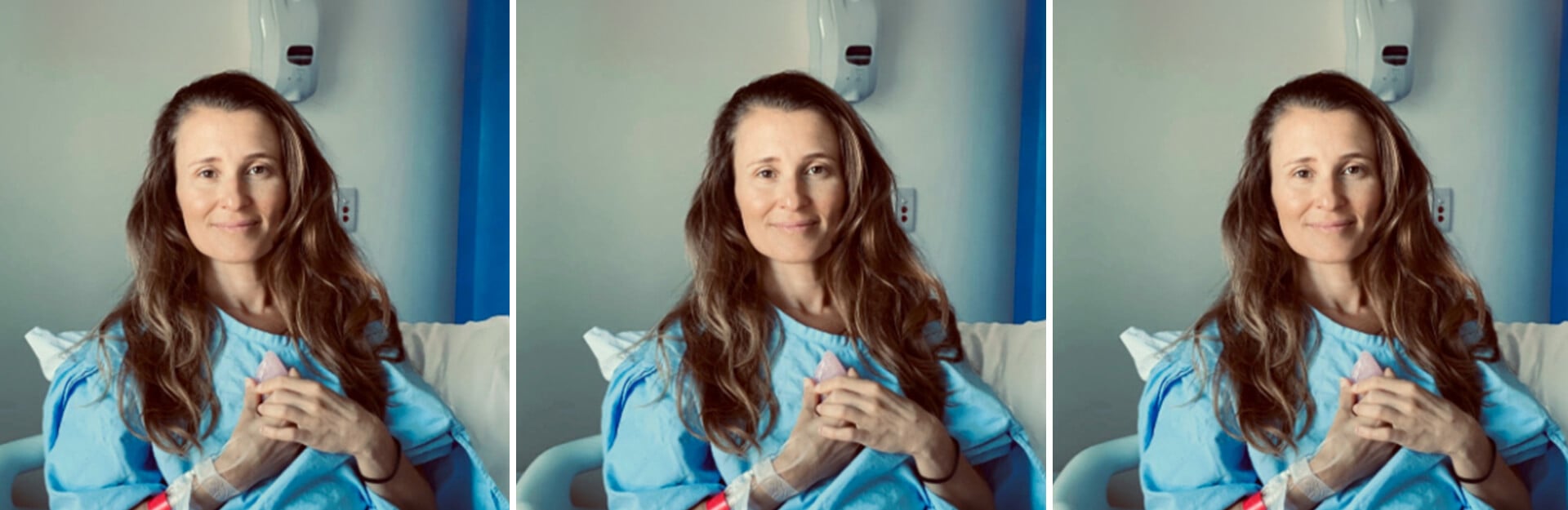 A woman with long hair wearing a hospital gown sits on a bed, smiling confidently at the camera.