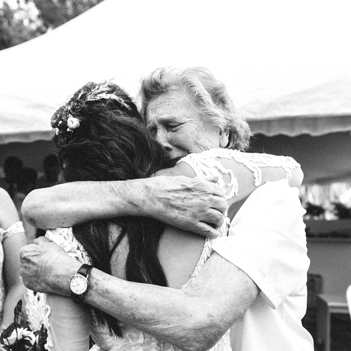 A young woman and an elderly woman embrace, both showing emotion, in a candid moment at an outdoor event.