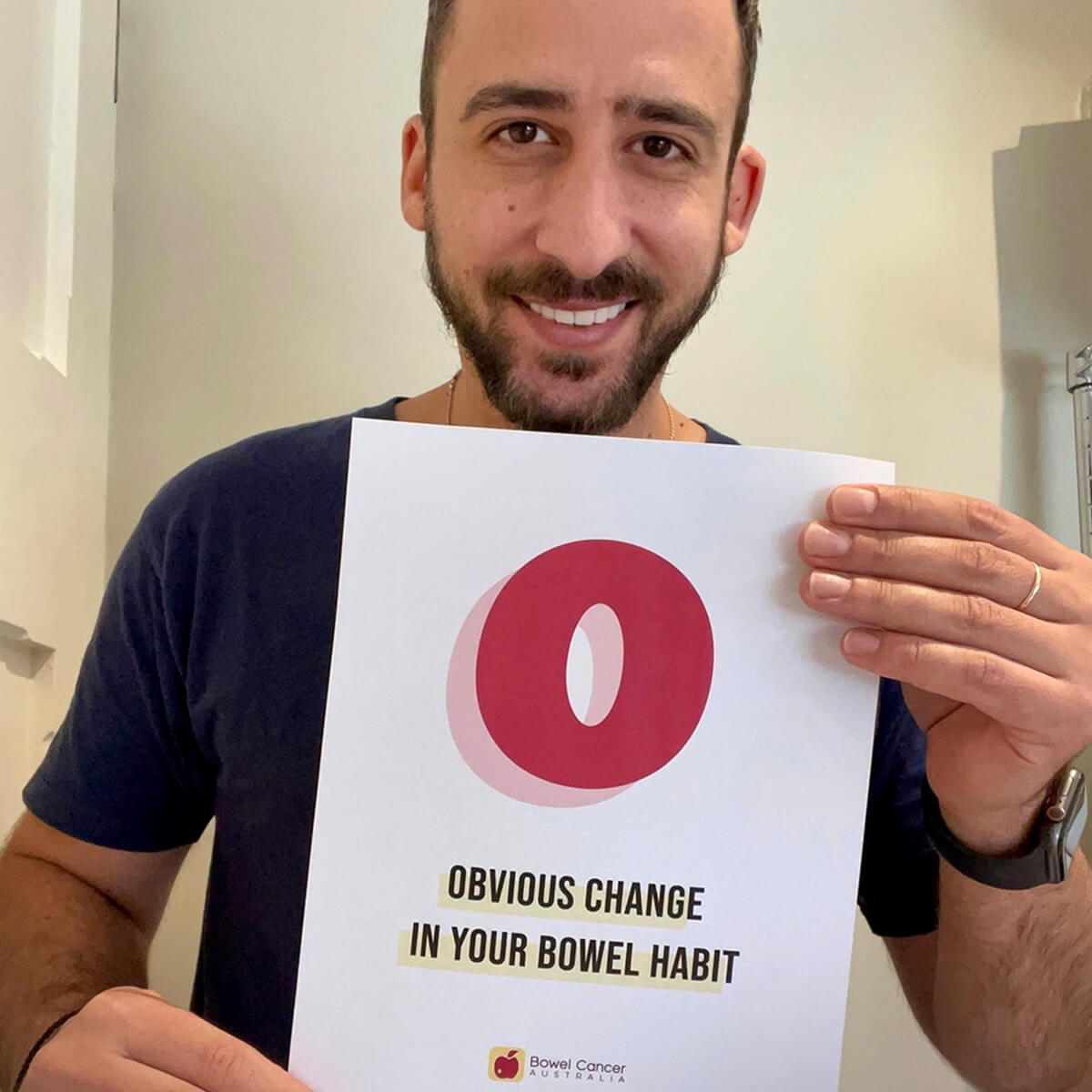A man holds a sign that reads "0 OBVIOUS CHANGE IN YOUR BOWEL HABIT," promoting awareness about bowel health.