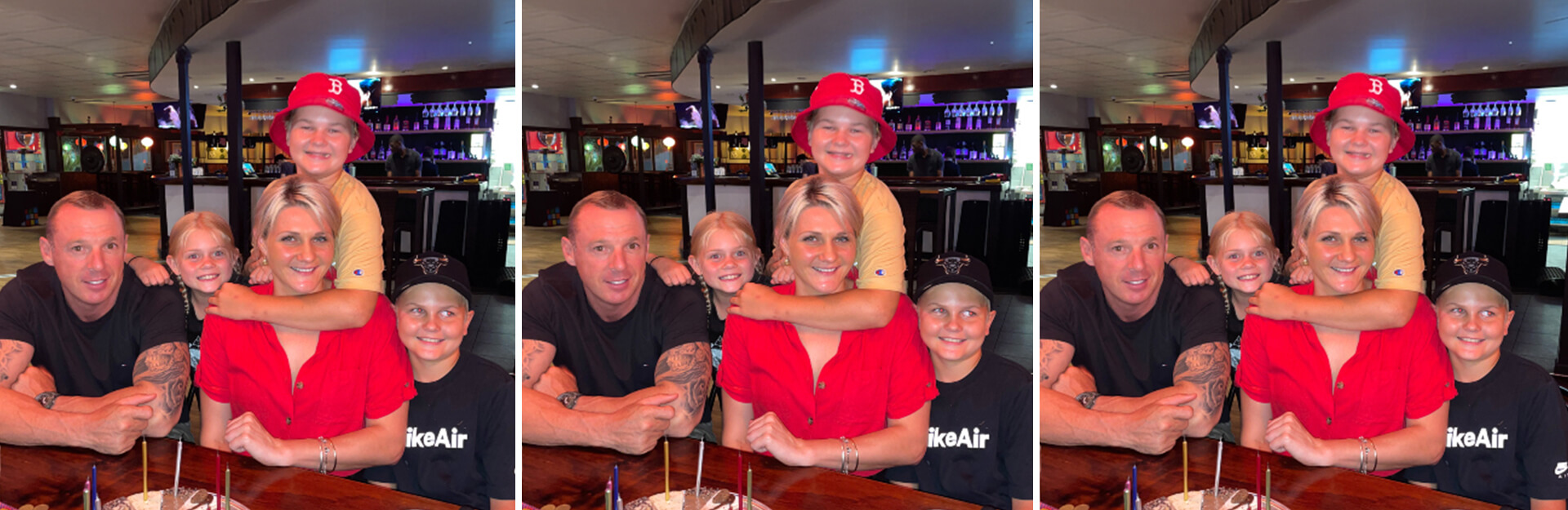 A family of four poses together in a restaurant, smiling, with drinks and desserts on the table in front of them.