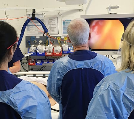 Medical professionals in scrubs observe a monitor displaying an endoscopic image during a colonoscopy.