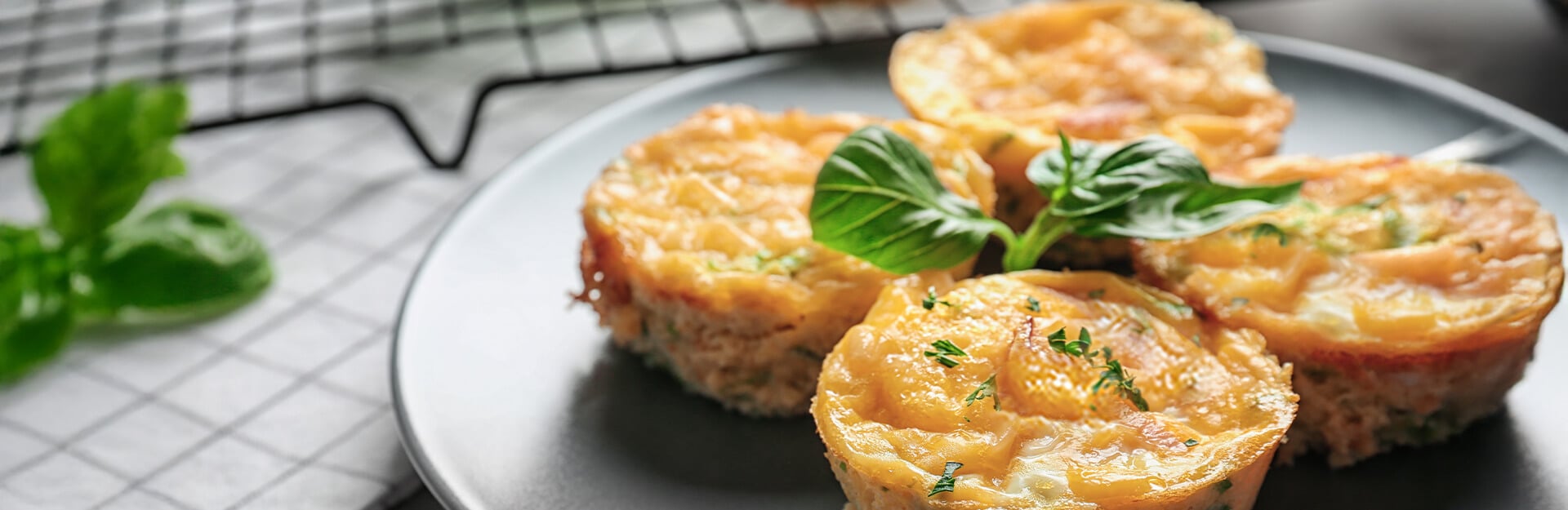 Four baked egg muffins topped with herbs, served on a gray plate with a sprig of basil.