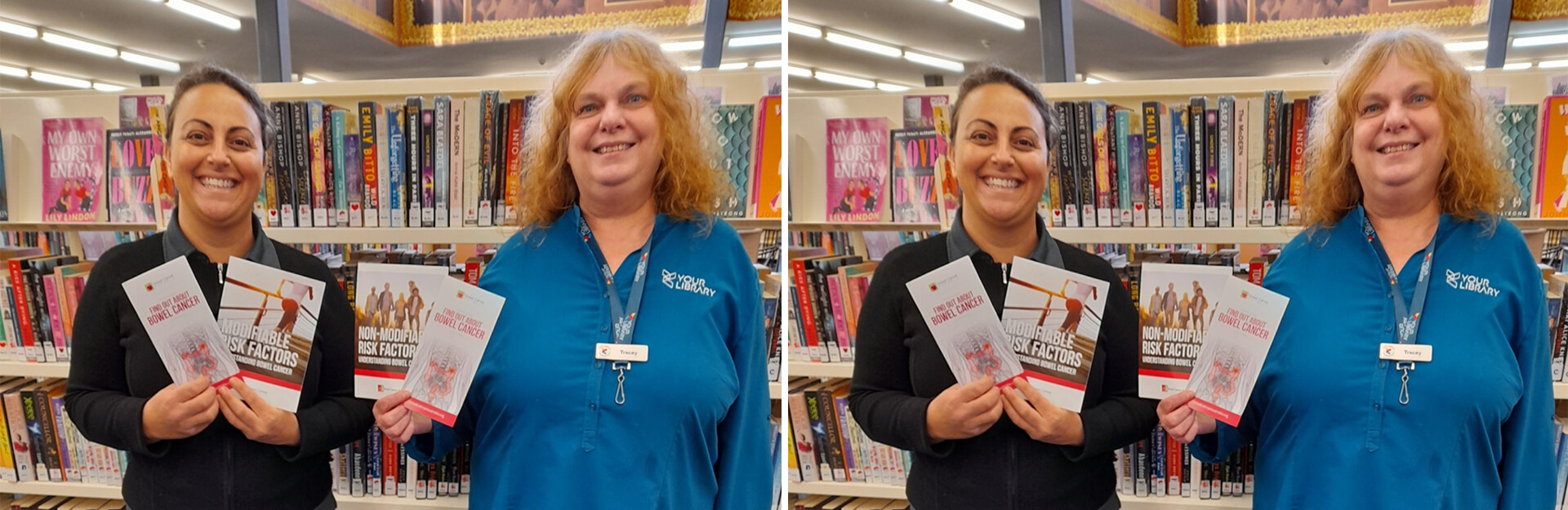 Two women smile while holding brochures about bowel cancer in a library, with shelves of books in the background.