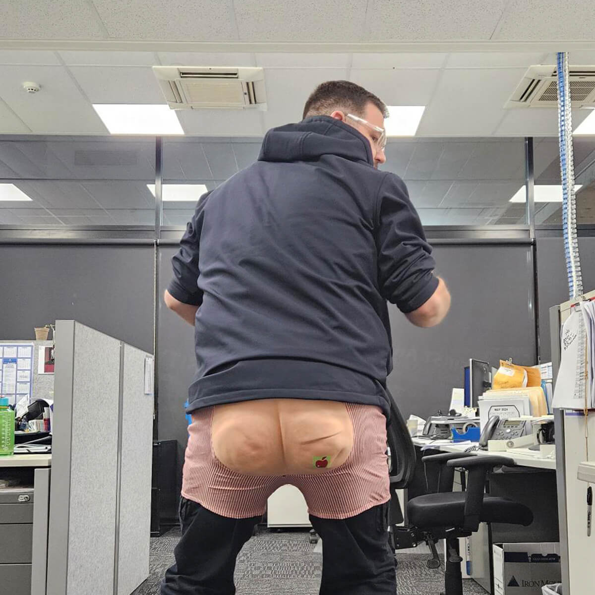 A person in an office setting is wearing a novelty apron with a cartoonish butt design.