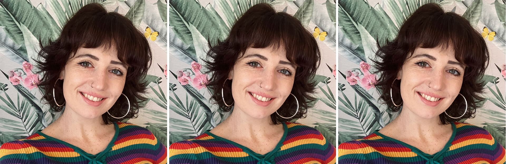 A smiling woman with curly hair and hoop earrings poses in front of a tropical plant backdrop, wearing a striped top.