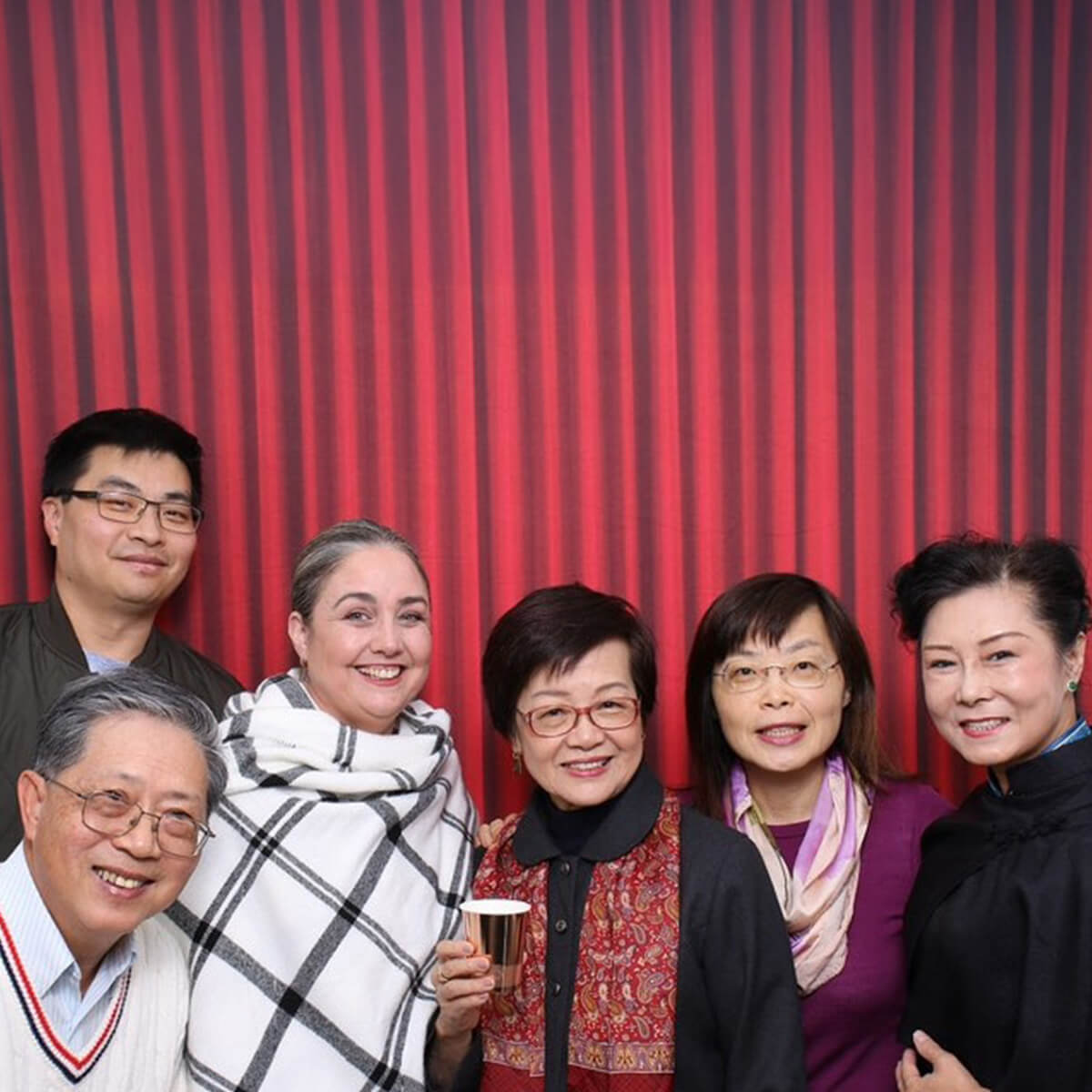 A group of six people smiling together in front of a red striped backdrop.