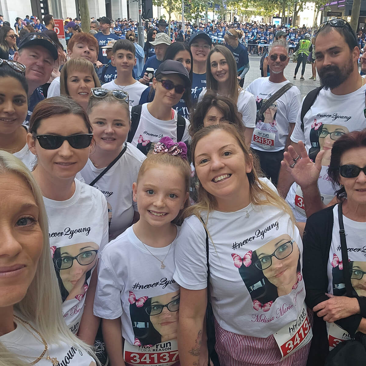 A group of people wearing matching shirts with a photo and text, smiling at the camera during an event.