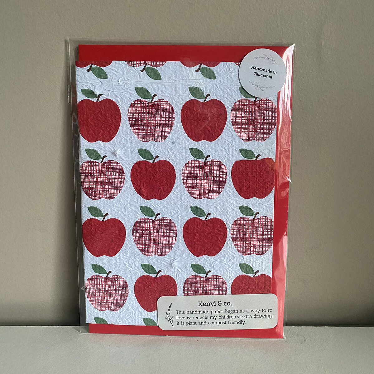 A card featuring a pattern of red apples on white paper with a label stating "Handmade in Tasmania" and product details.
