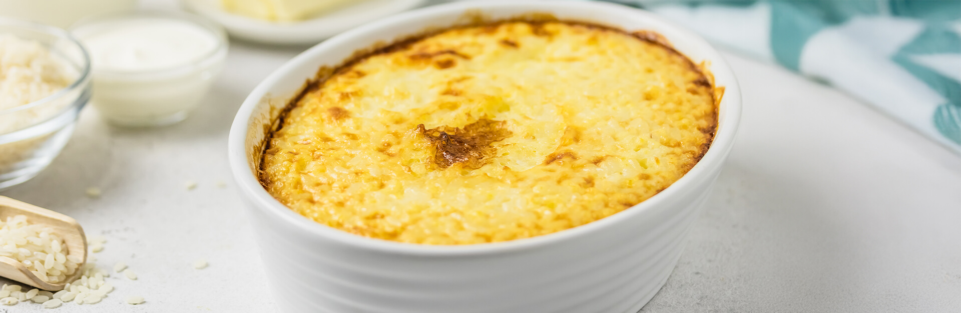 A baked dish with a golden, crispy top, surrounded by bowls of rice and cream.