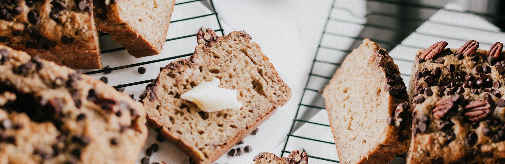 Sliced bread with chocolate chips and pecans on a cooling rack, with a pat of butter on one piece.