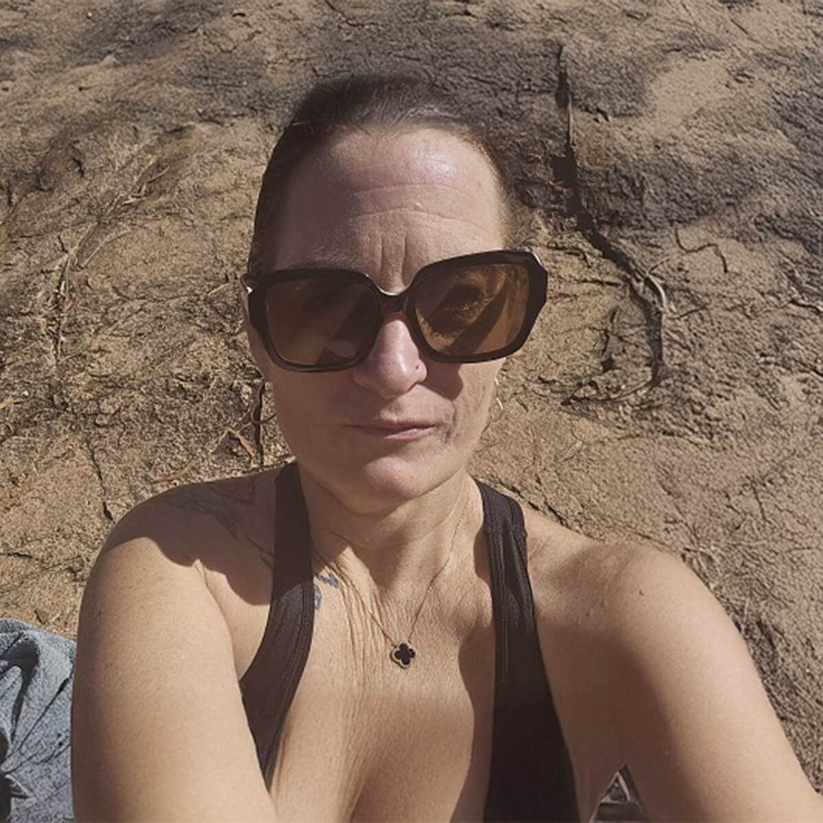 A woman with sunglasses poses for a selfie against a rocky background.