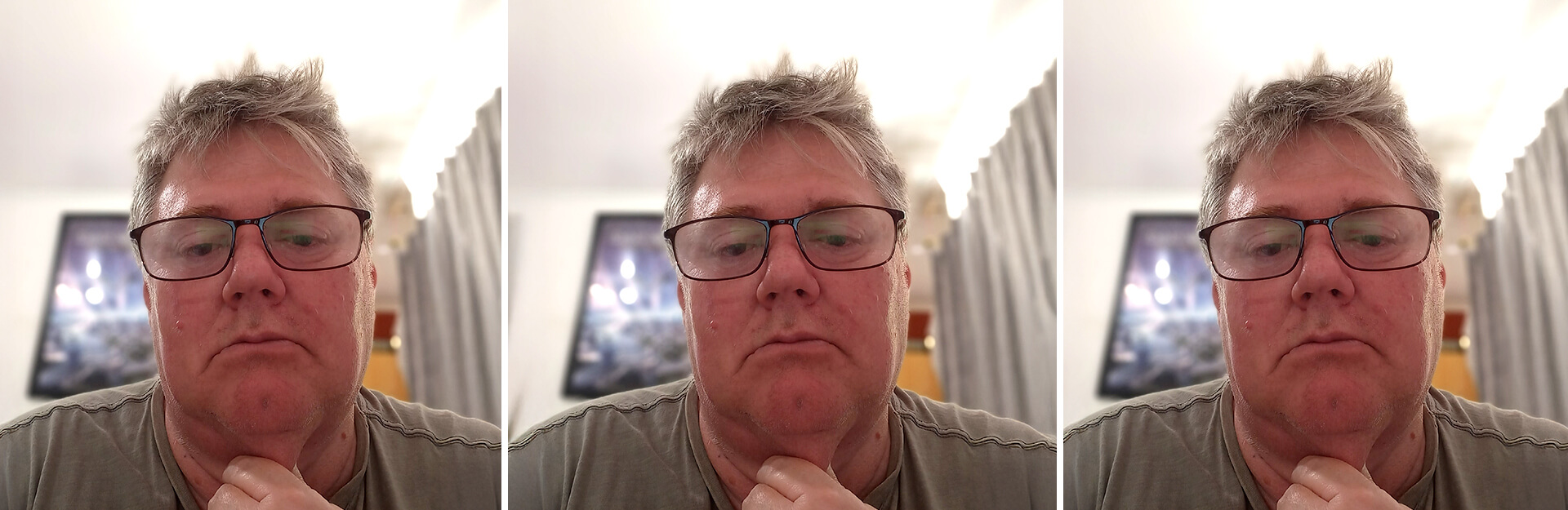 A middle-aged man with glasses looks serious, resting his chin on his hand, in a room with curtains and artwork.