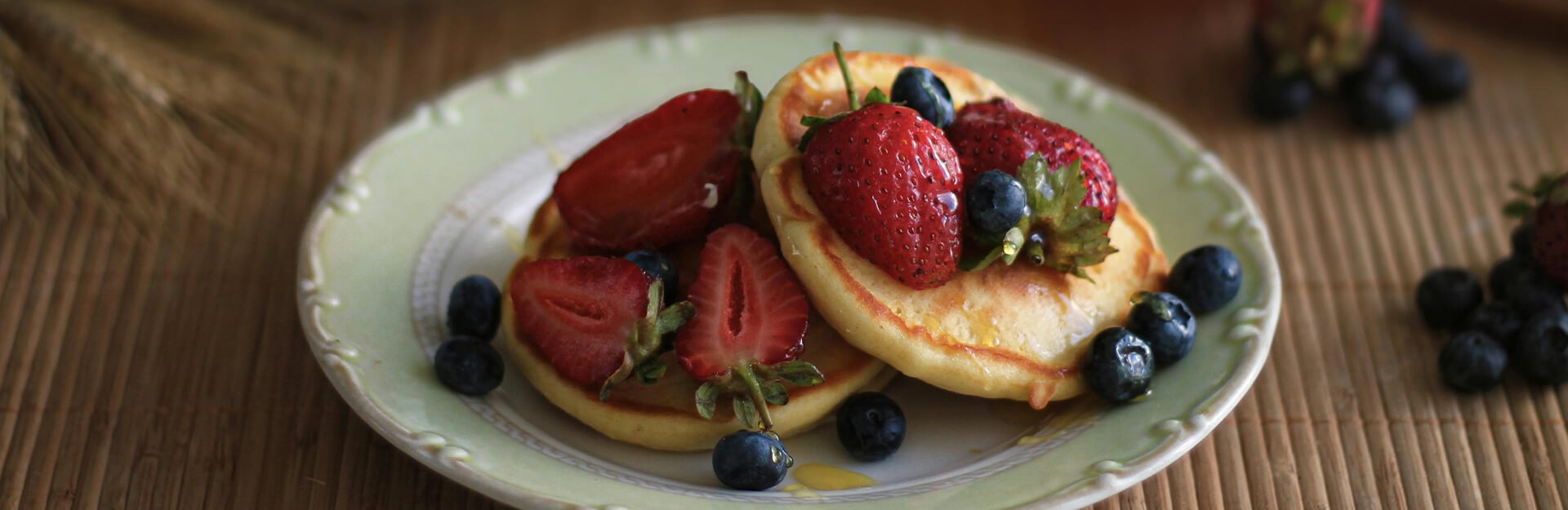 A plate of pancakes topped with strawberries and blueberries, drizzled with syrup, on a textured surface.