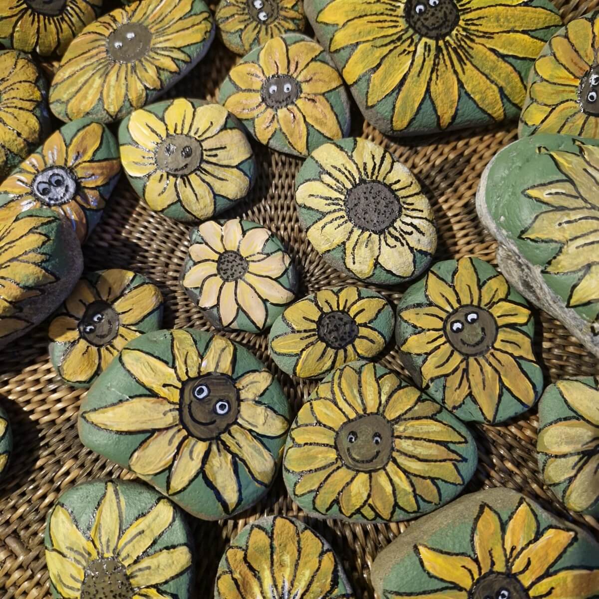 A collection of painted rocks featuring cheerful sunflowers with smiling faces on a woven surface.