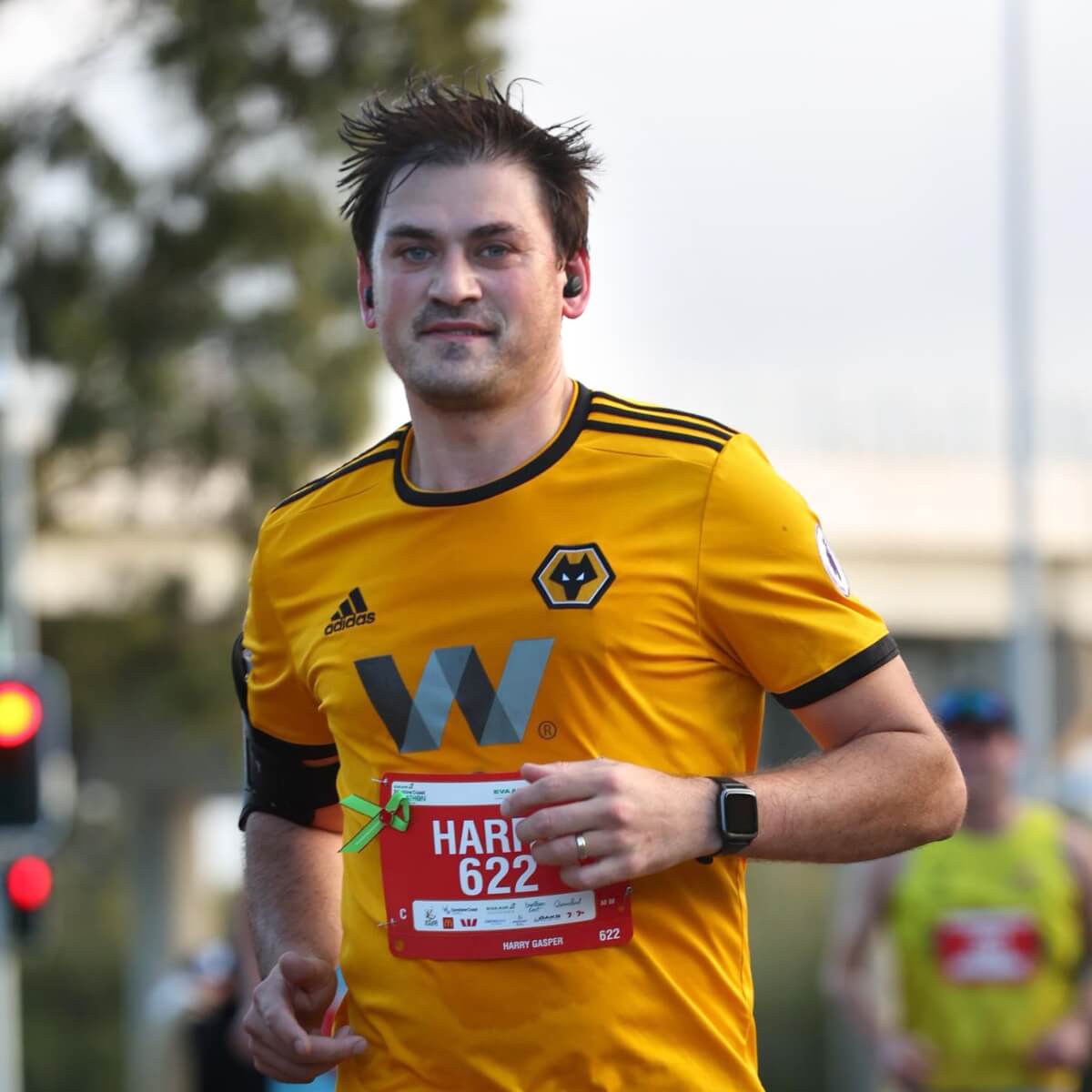 A man in a yellow sports jersey runs in a race, wearing earbuds and a race bib with the name "Harry" and number "622."