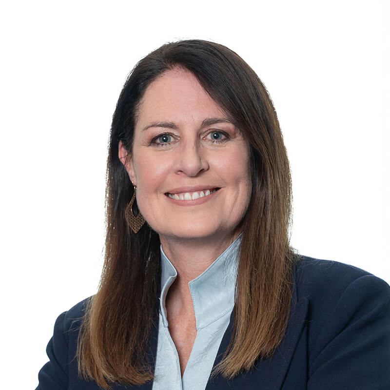 A smiling woman with long dark hair, wearing a blue blazer and light blue shirt, against a white background.
