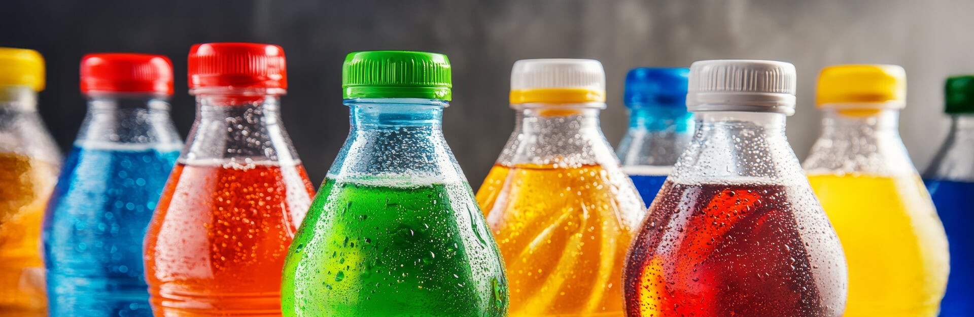 Colorful soda bottles with various flavors and condensation, arranged in a row against a blurred background.