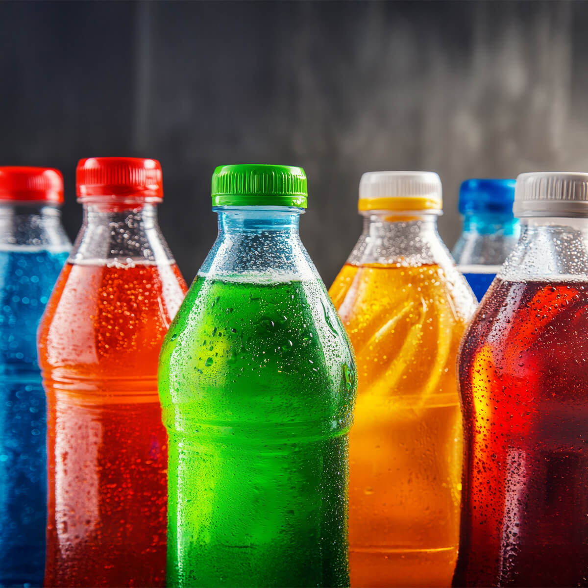 A lineup of colorful soda bottles with condensation, featuring red, blue, green, orange, and yellow caps.