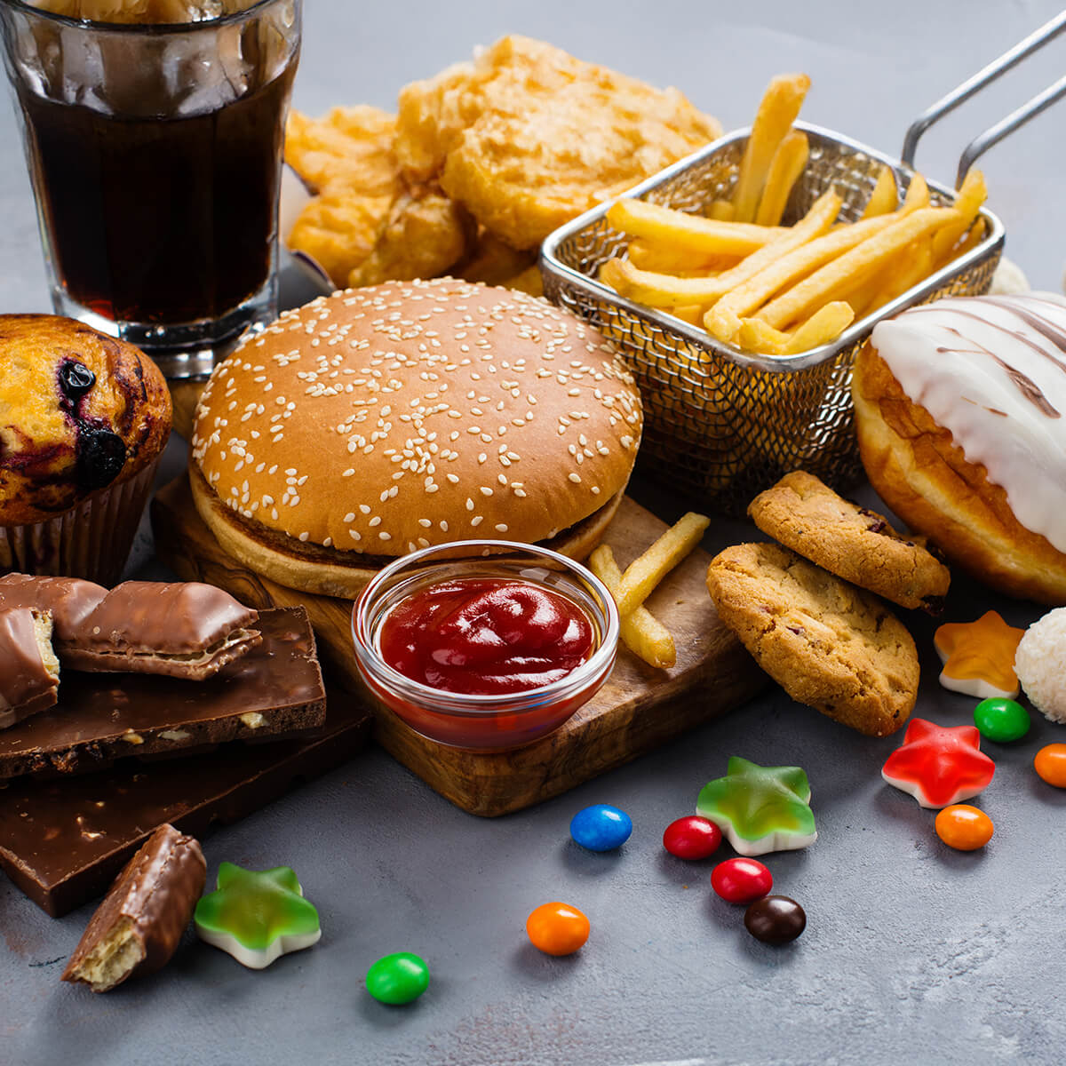 A variety of fast food items including a burger, fries, chicken, donuts, cookies, candy, and a drink.