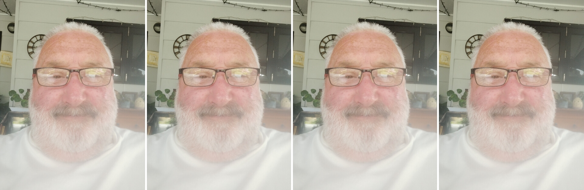 A smiling man with a beard and glasses, sitting indoors with plants and decorative items in the background.