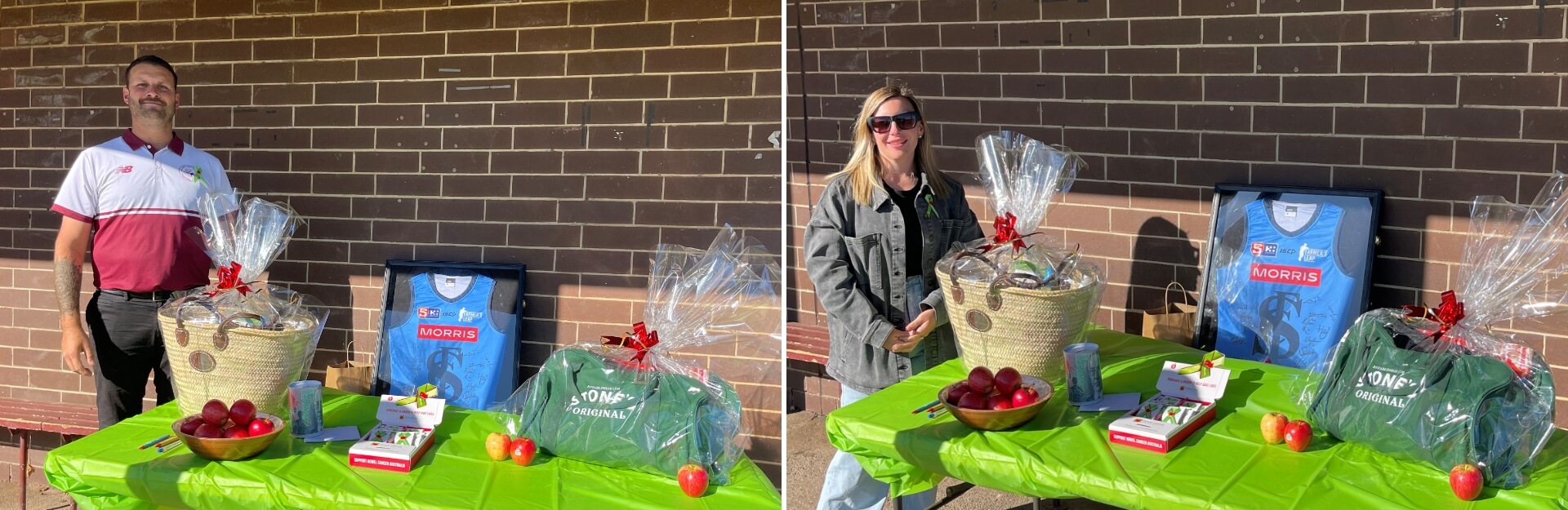 A man and woman stand beside a table with gift baskets, a signed jersey, and apples, set against a brick wall.