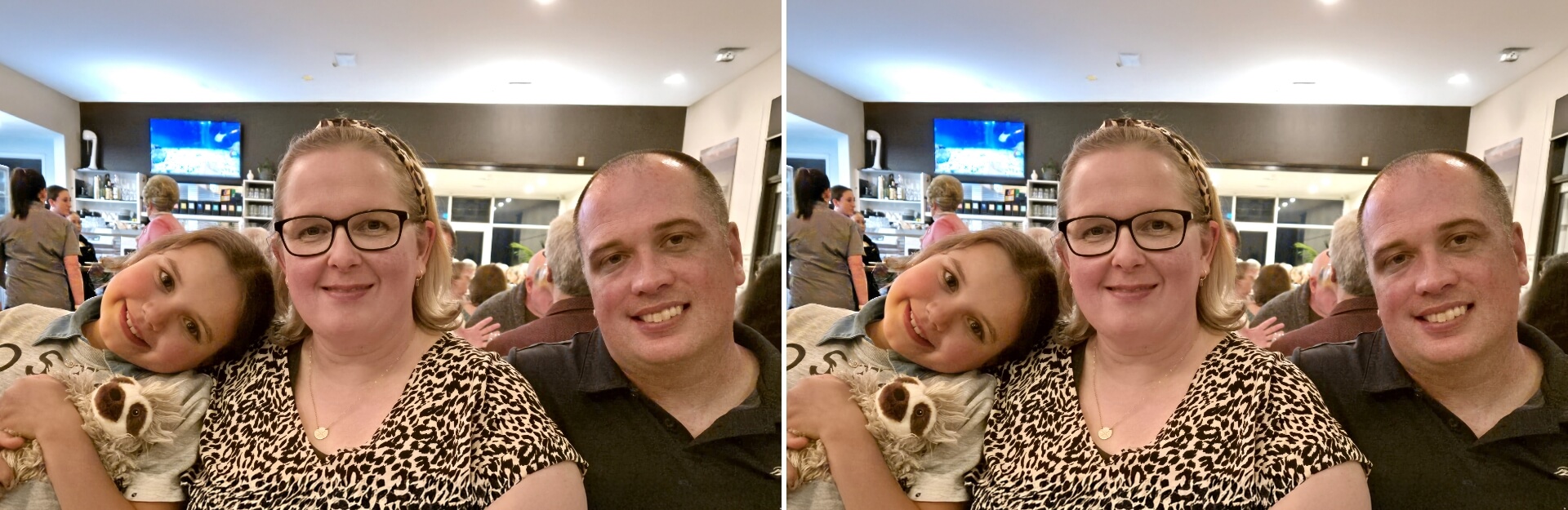 A woman, a girl holding a toy sloth, and a man smile together in a restaurant setting with people in the background.