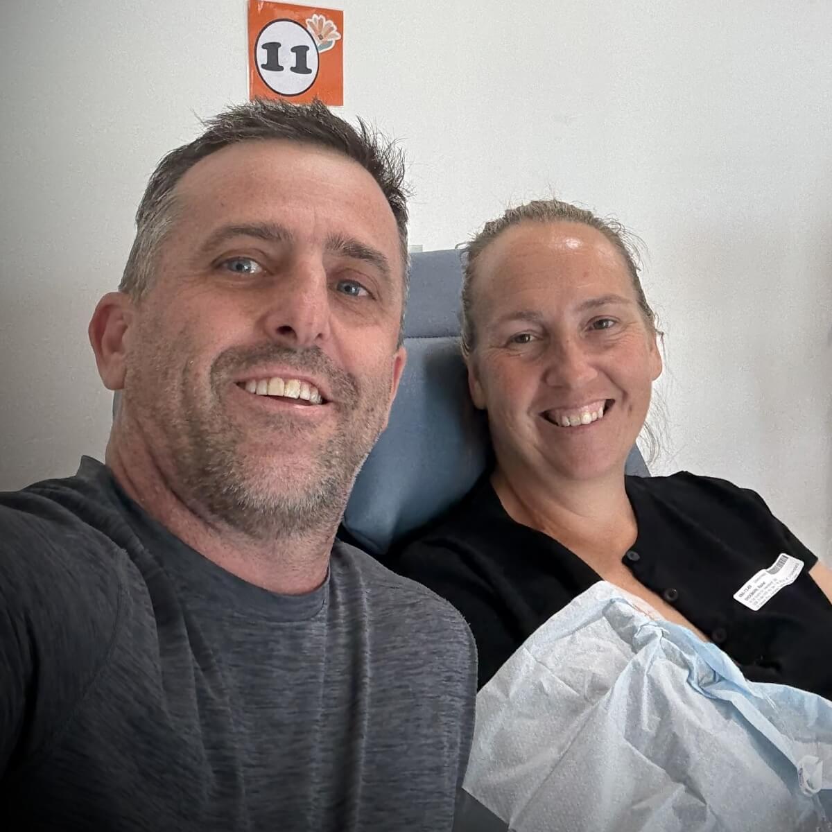 A man and a woman smiling together in a medical setting, with a number 11 sign visible in the background.