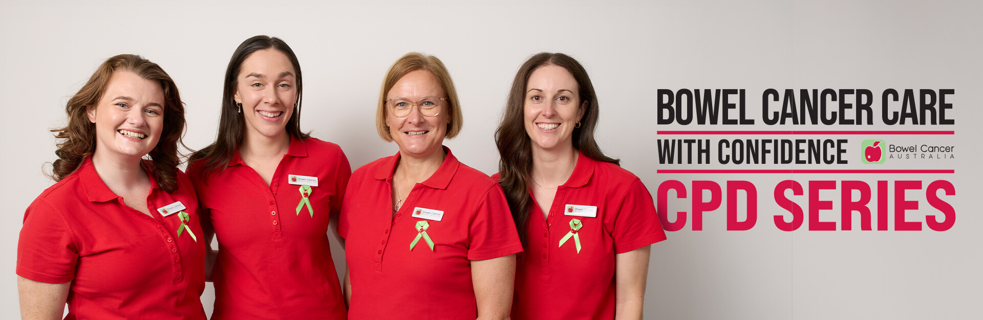 Four women in red polo shirts stand together, smiling, with a banner promoting bowel cancer care.