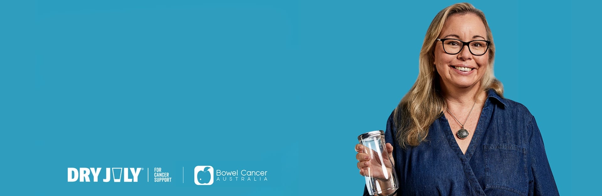 A smiling woman in a denim shirt holds a glass jar against a bright blue background, promoting Dry July for cancer support.