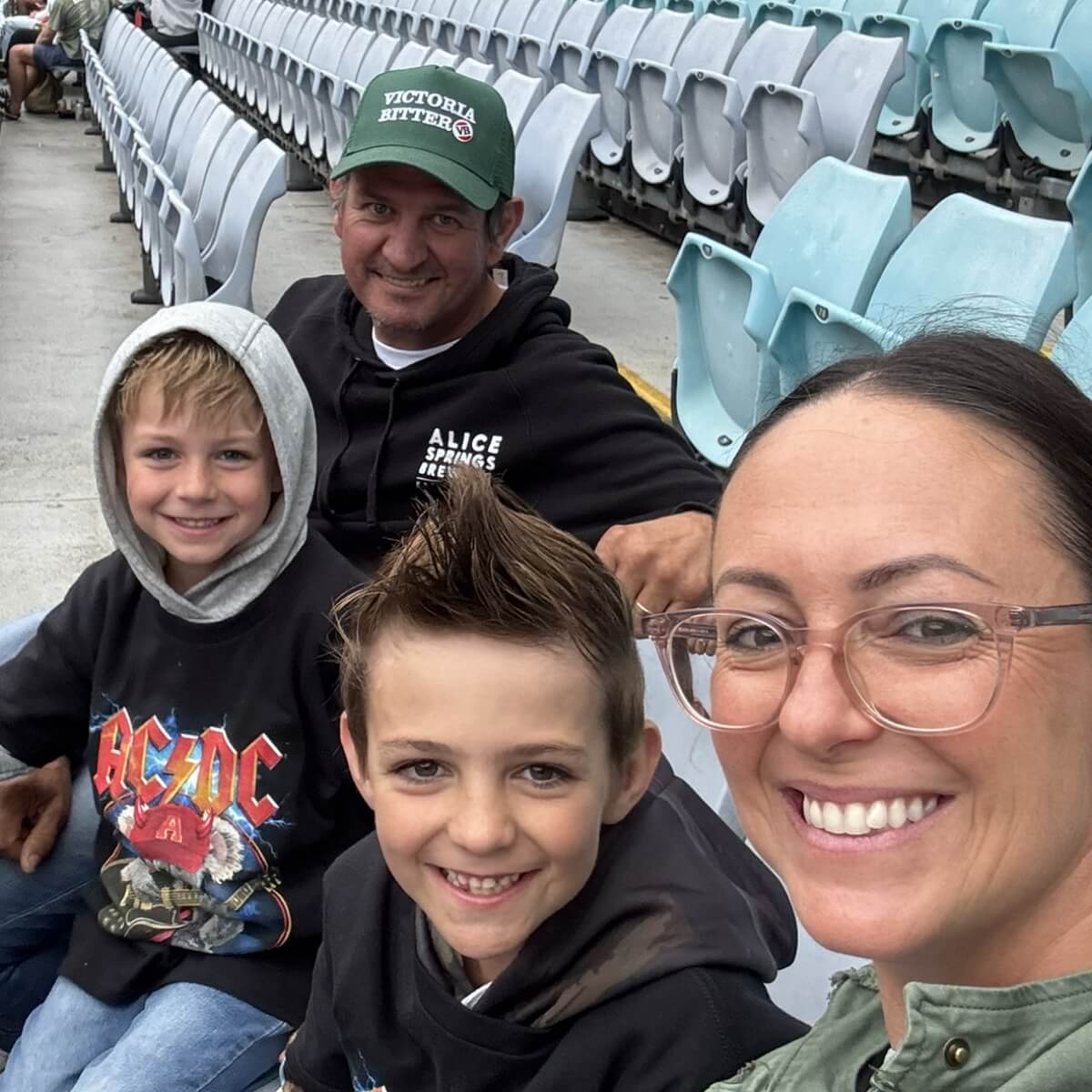 A smiling family of four, including two boys, a man, and a woman, sitting in stadium seats.