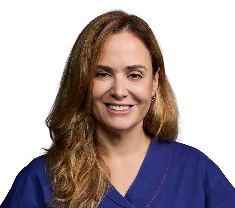 Smiling woman with long brown hair, wearing a blue medical scrub top, against a white background.