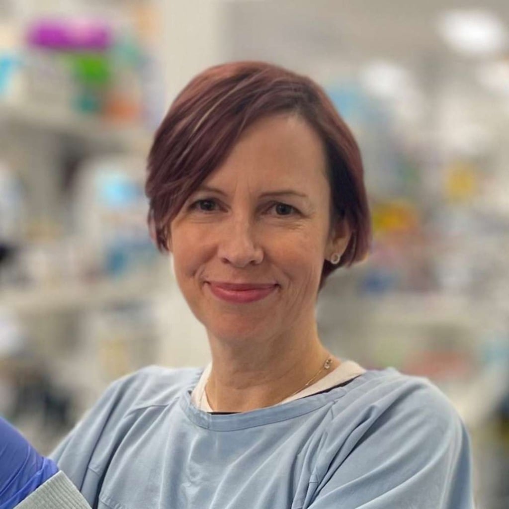 A smiling woman in a lab coat stands in a research environment, representing the early-onset bowel cancer centre of research excellence.