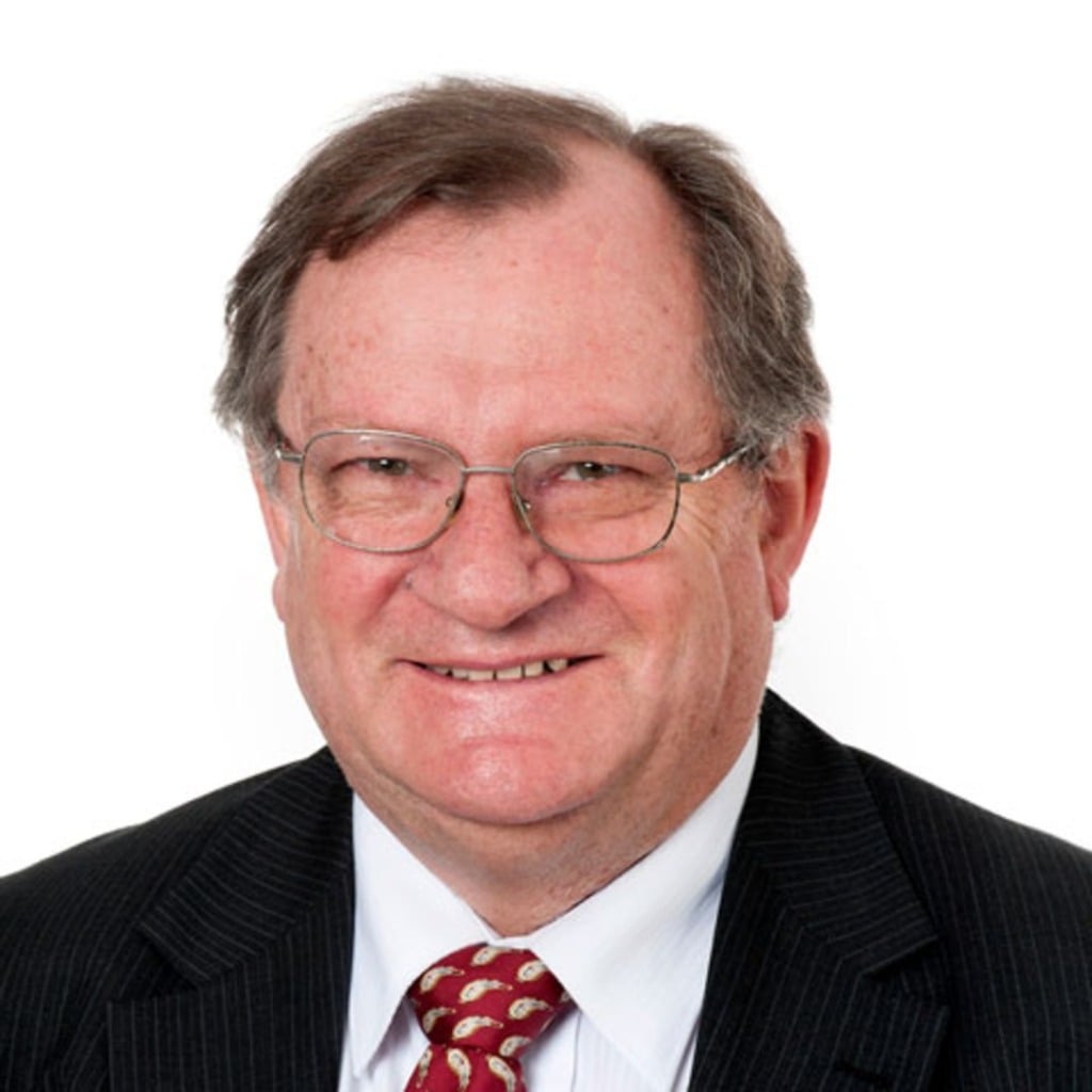Portrait of a man with glasses, wearing a suit and tie, smiling against a plain white background.