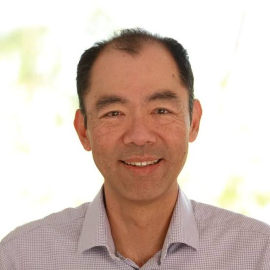 A smiling man in a collared shirt, with a blurred outdoor background, representing the early-onset bowel cancer centre of research excellence.