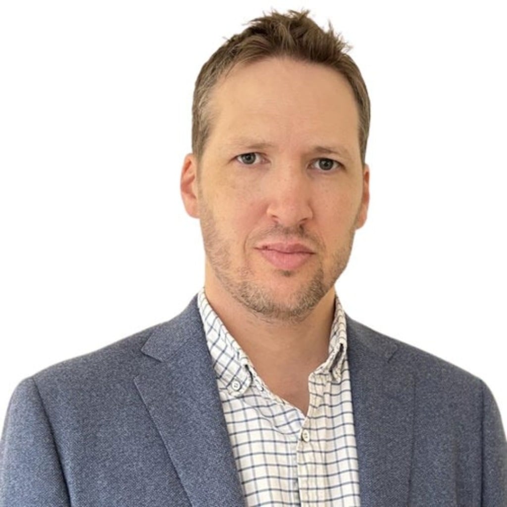 A man in a blazer and checked shirt poses against a white background, representing the early-onset bowel cancer centre of research excellence.