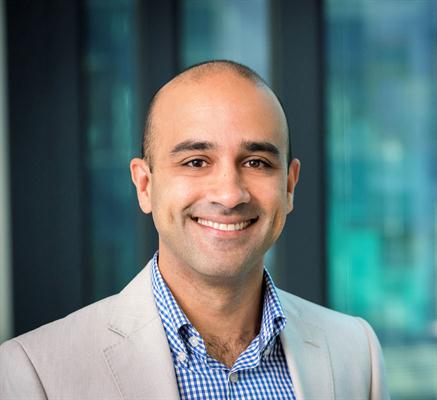 Smiling man in a light suit and checkered shirt, standing in front of a glass background, representing early-onset bowel cancer centre of research excellence.