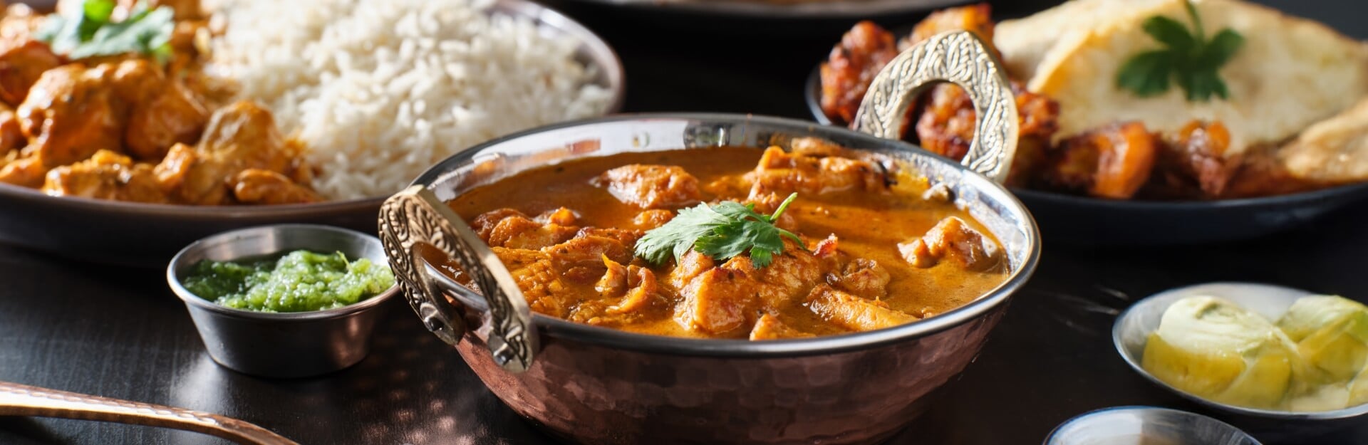 A bowl of mild Indian chicken curry garnished with cilantro, served with rice, green sauce, and lemon slices.