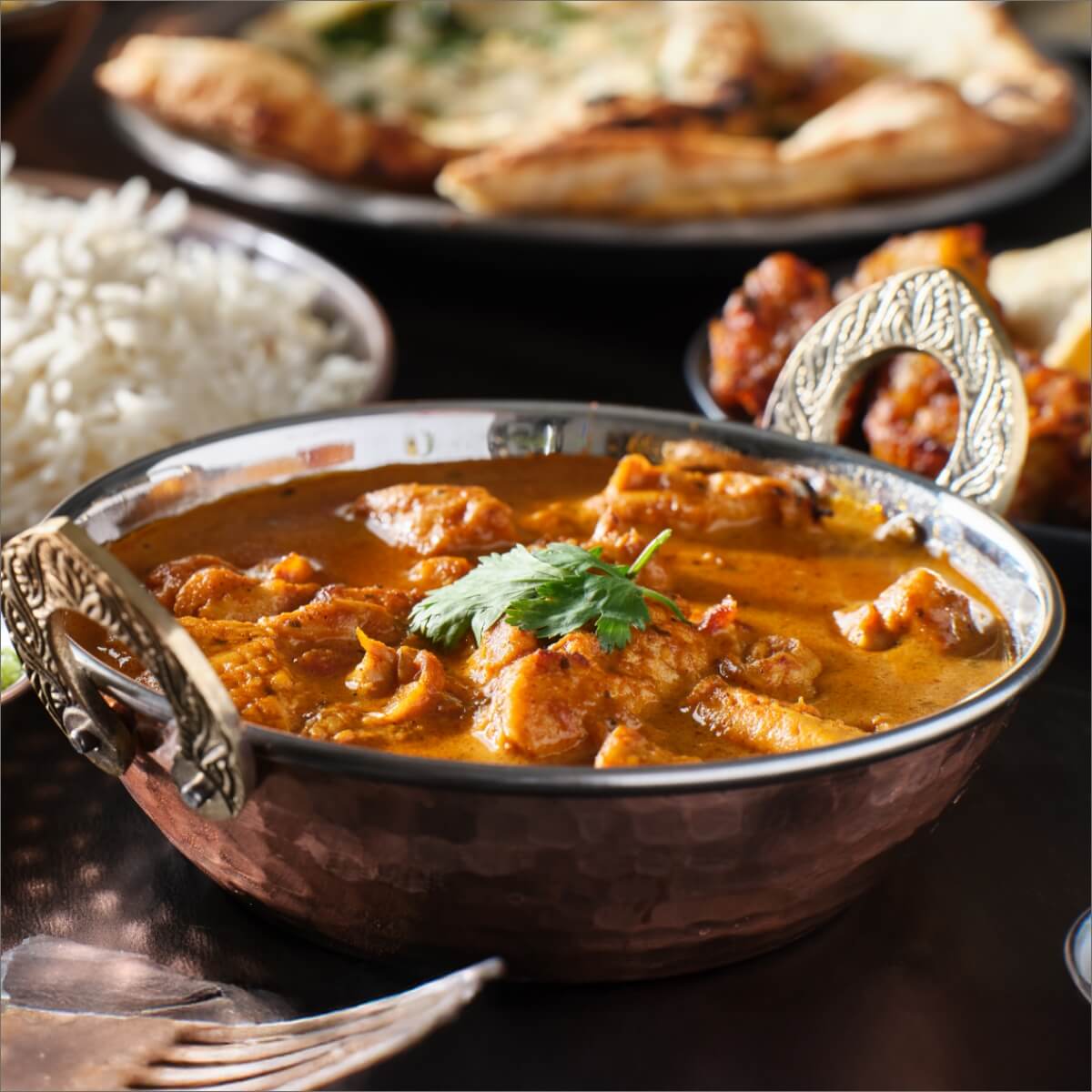 A bowl of mild Indian chicken curry garnished with cilantro, surrounded by rice and naan.