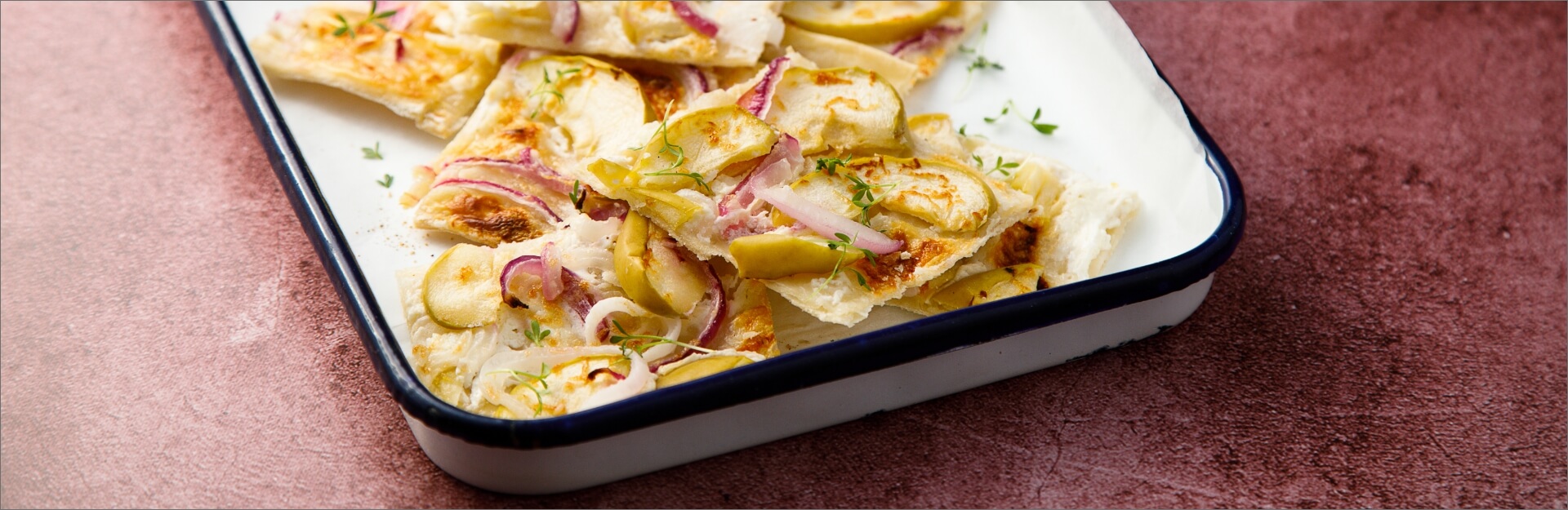 A serving of apple, onion, and goat cheese tart on a white dish, garnished with herbs.