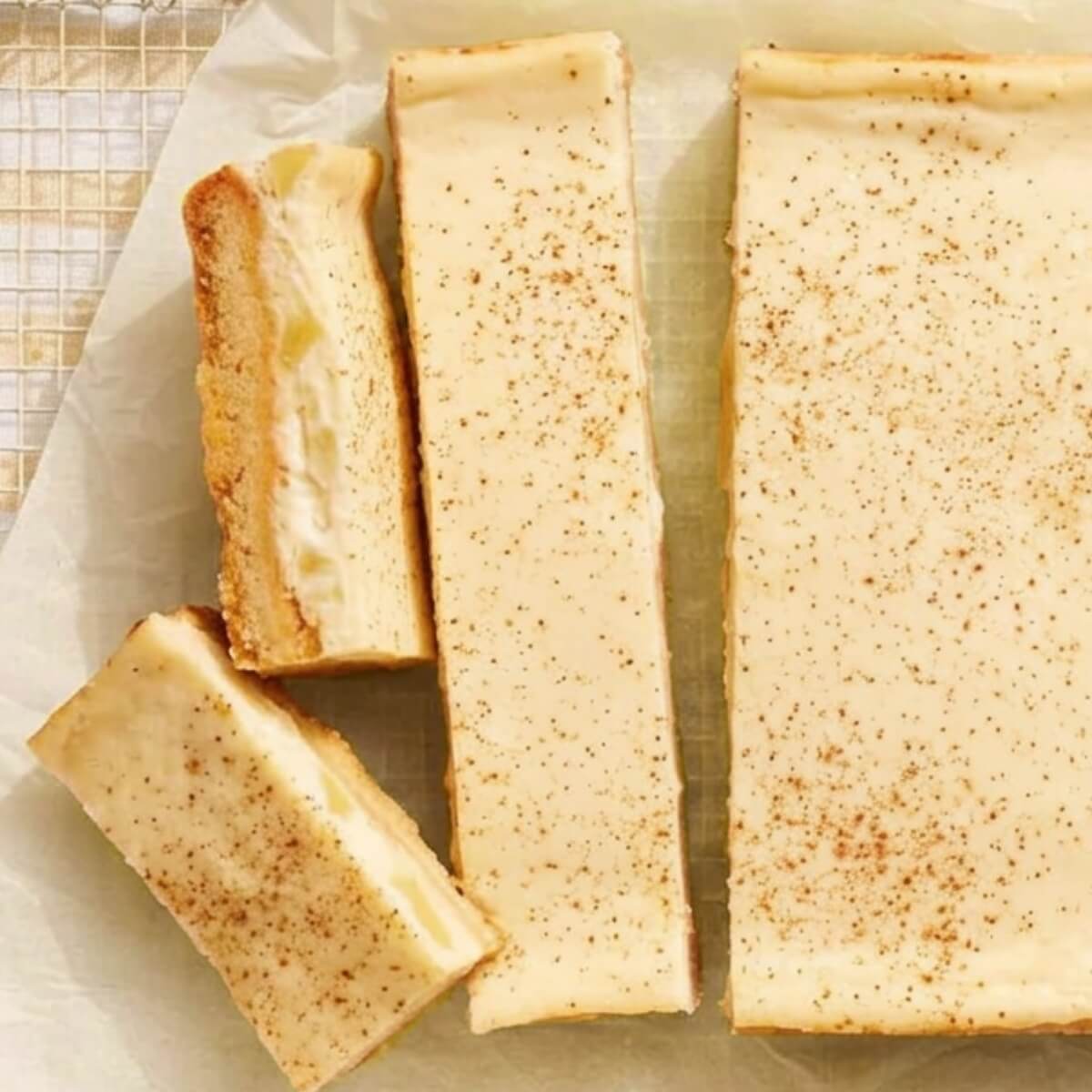 Three slices of apple and sour cream dessert with a smooth, creamy topping and a sprinkle of cinnamon on parchment paper.