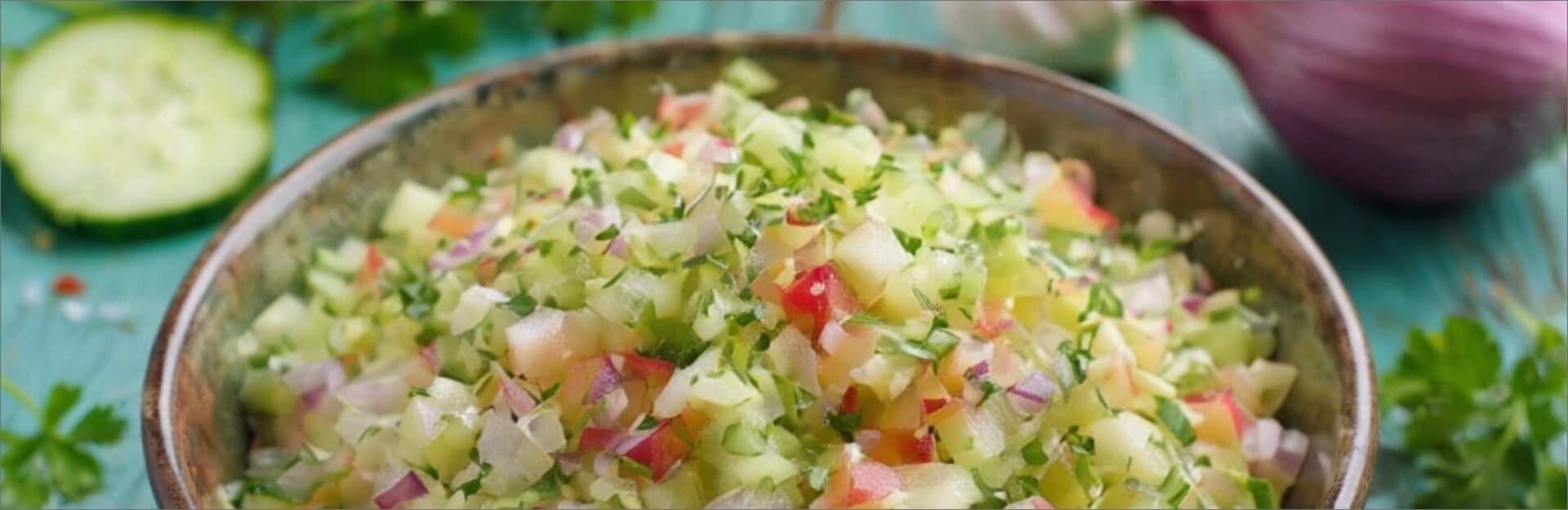 A bowl of crunchy apple slaw with diced apples, cucumbers, and herbs, garnished with red onion, on a wooden surface.