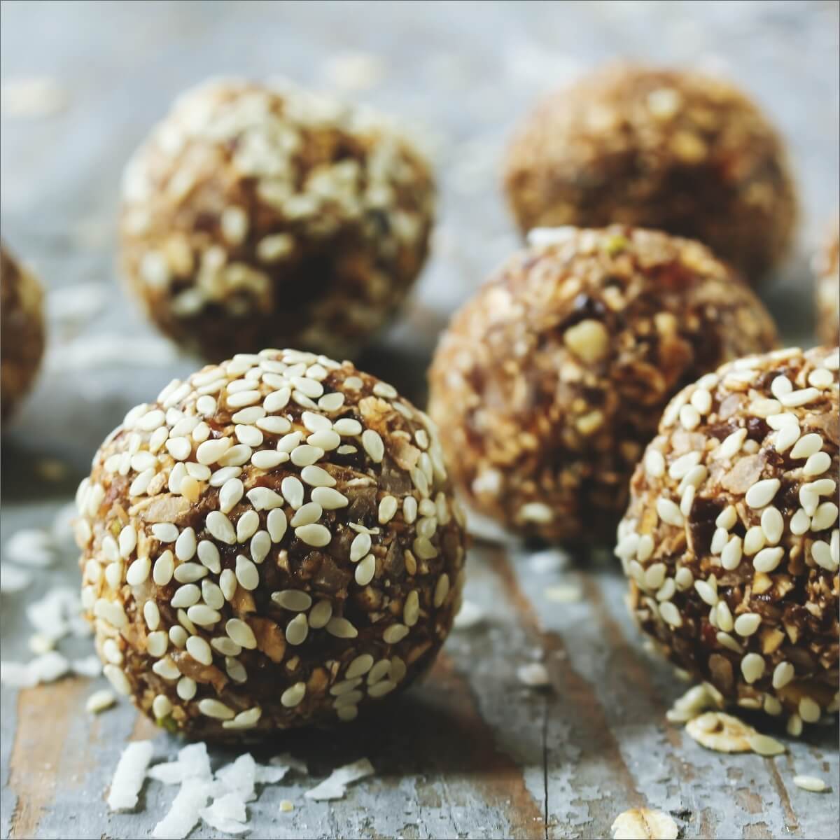 A close-up of protein balls coated in sesame seeds on a rustic wooden surface.
