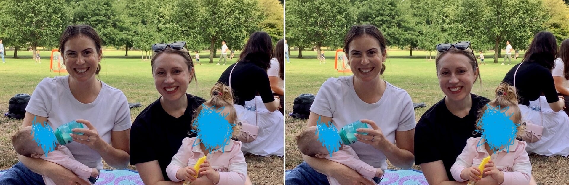 Two women sitting on grass, one holding a baby, both smiling, with a park setting in the background.
