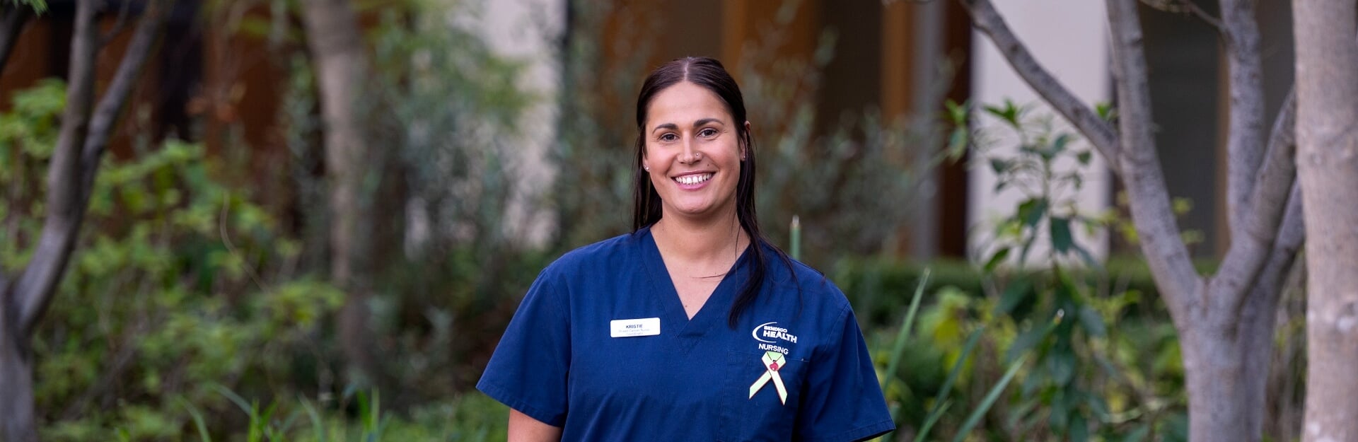 A smiling nurse in a blue uniform stands outdoors with greenery in the background, representing hope for bowel cancer patients.