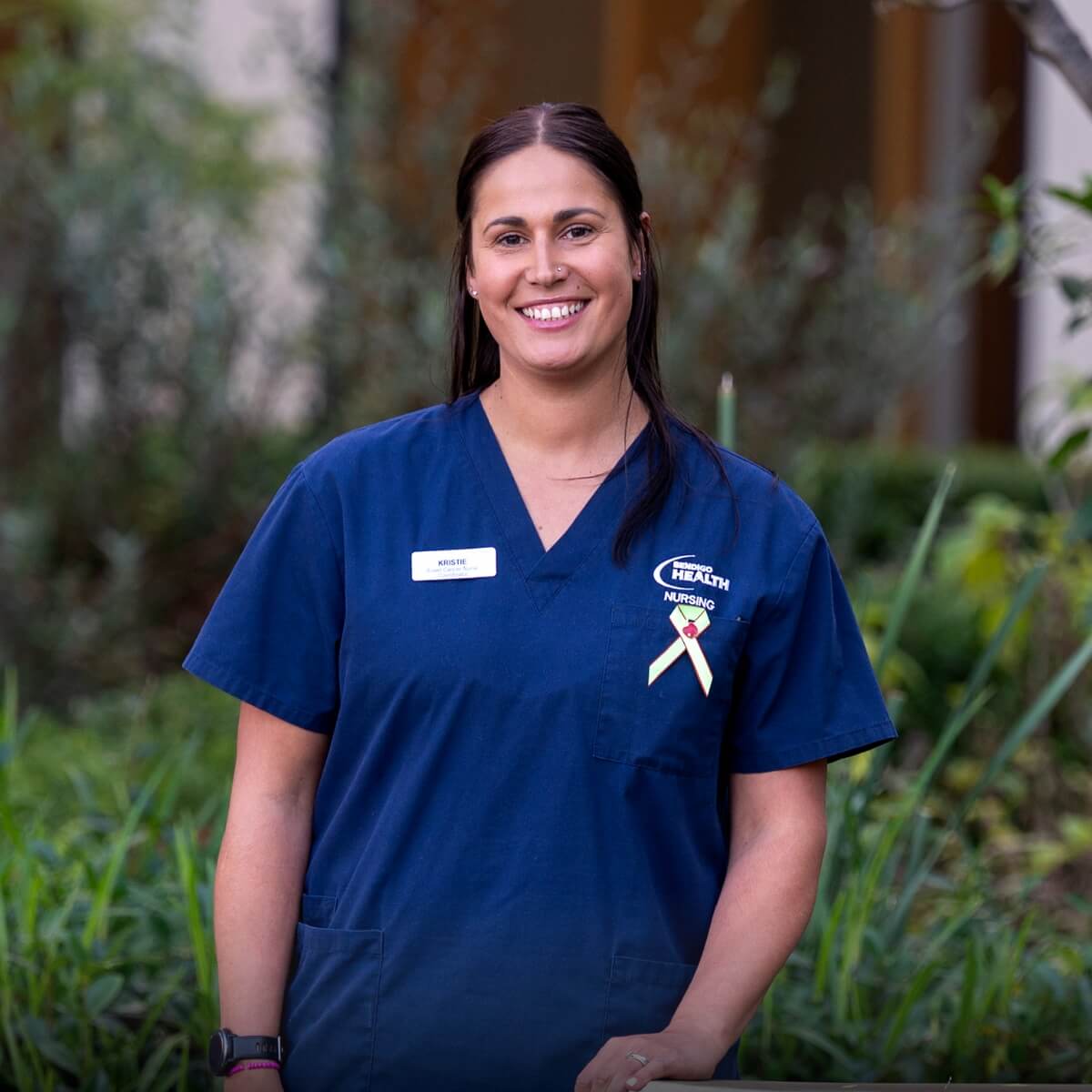 A nurse in a blue uniform smiles outdoors, promoting "Driving hope for bowel cancer patients."