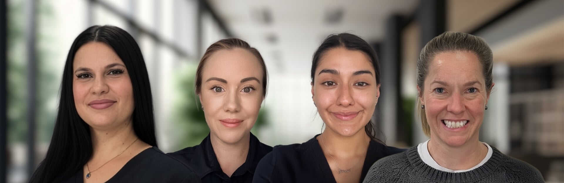 Four women are smiling, standing side by side in a bright, modern indoor setting.